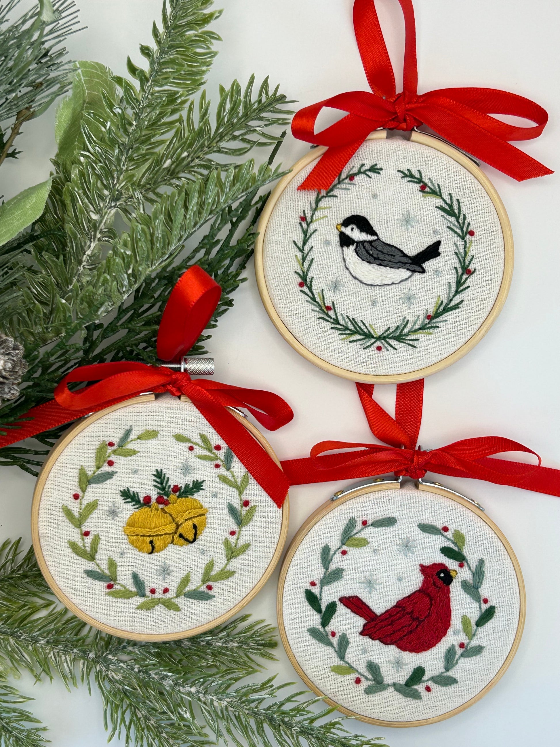 Three embroidered hoop ornaments kit with red ribbons featuring birds and bells and greenery, designed by Deb Strain.  