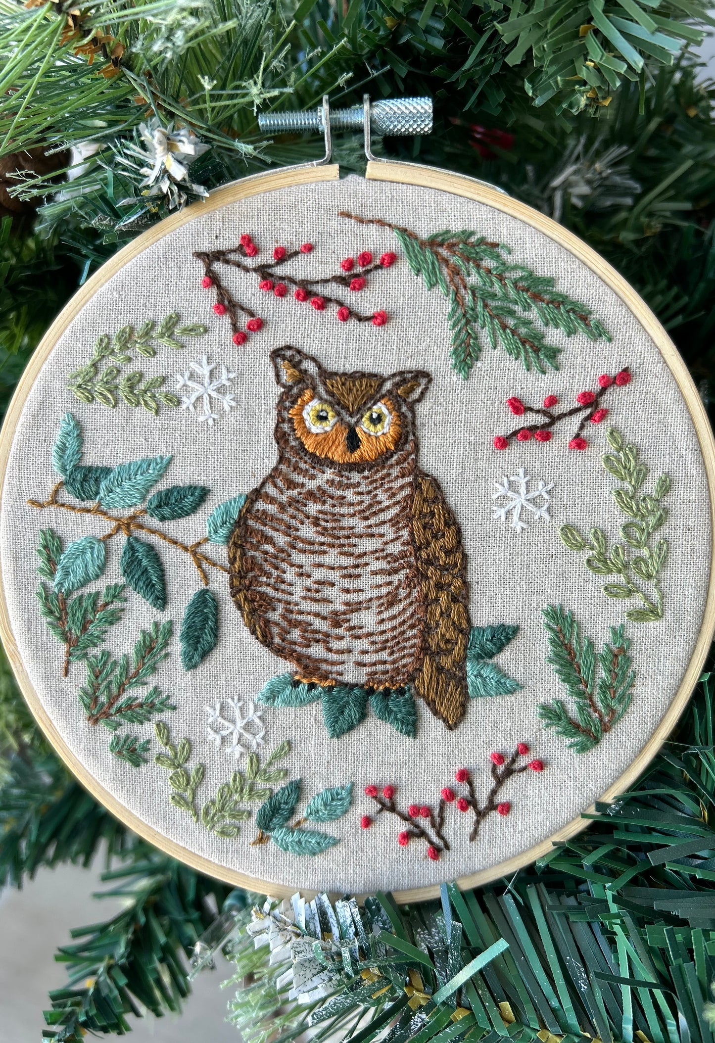 An embroidery kit depicting an owl surrounded by foliage and berries, displayed in a 6-inch hoop designed by Deb Strain.